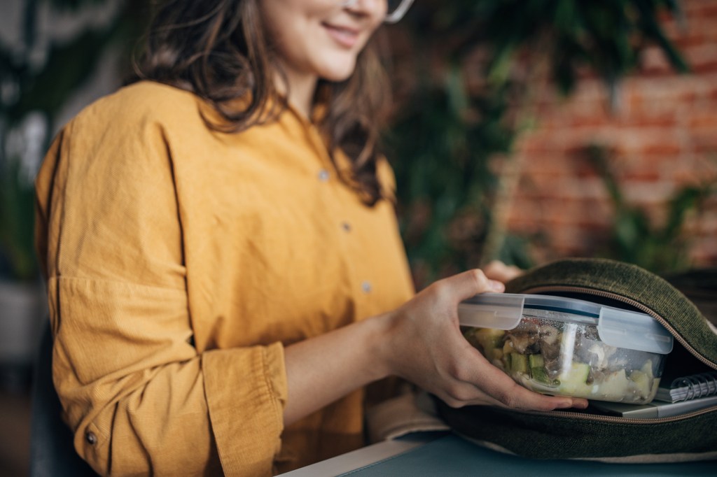 Young woman putting a lunch box in her backpack at home