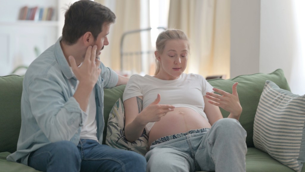 Upset pregnant couple arguing at home